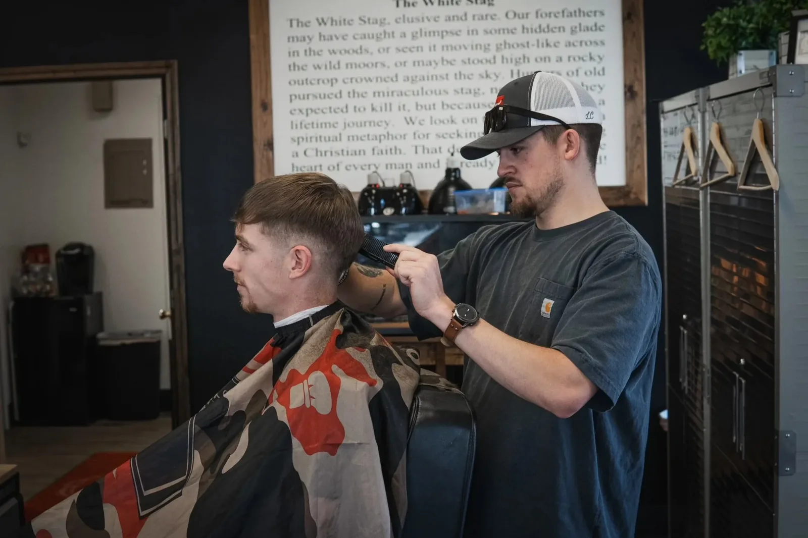 Reed cutting hair beneath the framed White Stag legend